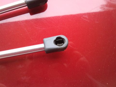 1998 Ford Crown Victoria - Two hood struts are shown resting on a red surface, with one in focus showing its attachment point.
