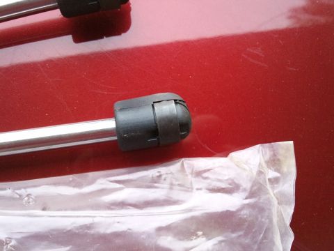 1998 Ford Crown Victoria - A hood strut is shown against a red metallic background, with a portion of its packaging in the foreground.