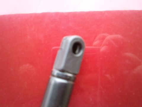 1998 Ford Crown Victoria - A close-up view of a metal hood holder part, likely for a vehicle, shown against a red background.