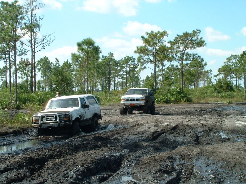 Two white Ford Broncos stuck in mud, one in foreground with brush guard