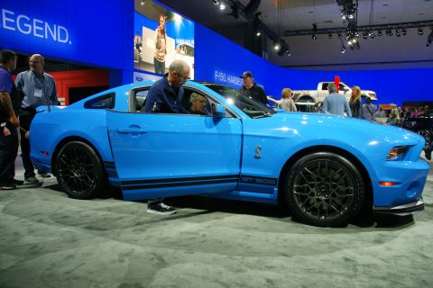 1993 Ford Taurus - A blue Ford Mustang GT 500 is displayed at an auto show with people looking at it.