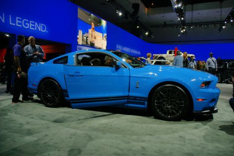 1993 Ford Taurus - A bright blue Ford Mustang GT500 is displayed at an auto show with people around it.