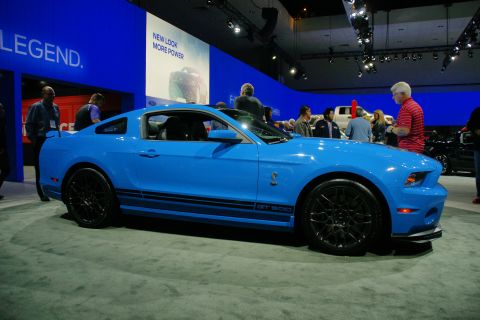 1993 Ford Taurus - A bright blue Ford Mustang Shelby GT500 is showcased at an auto show with people in the background.