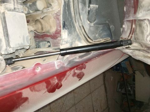 1998 Ford Crown Victoria - Close-up view of a hood strut installed on the inner panel of a red vehicle.