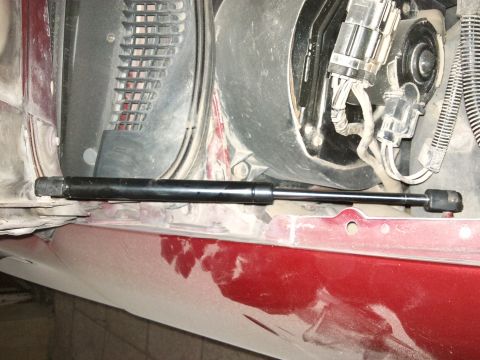 1998 Ford Crown Victoria - Close-up of a hood strut installed on the fender well of a red vehicle.