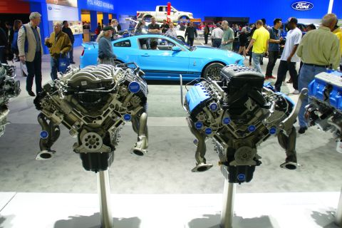 1993 Ford Taurus - Two V8 engines are displayed at an auto show, with a blue Ford Mustang visible behind them.