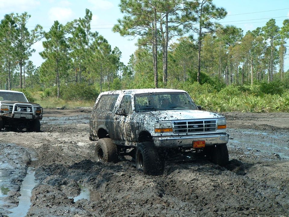 1995 Ford Bronco covered in mud, driving off-road with another vehicle behind it