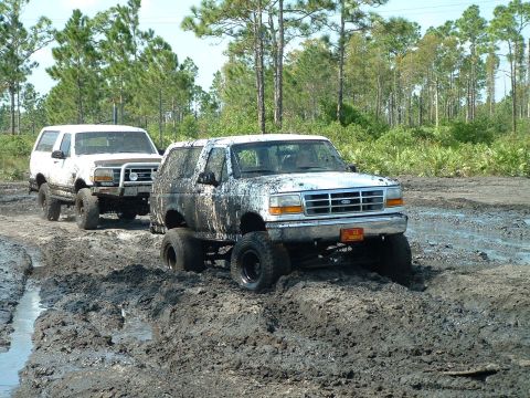 1995 Ford Bronco - Two Ford Broncos navigate a challenging muddy terrain, their off-road capabilities.