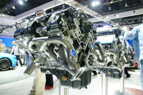 1993 Ford Taurus - A detailed cutaway view of an engine is displayed at an auto show, with people observing in the background.