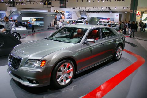 1993 Ford Taurus - A gray Chrysler 300 sedan is displayed indoors at an auto show with red accents on the floor.