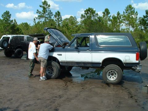 1995 Ford Bronco - Two Ford Broncos are in a muddy area, with people working on the engine of one.