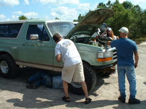 1995 Ford Bronco - Three people attend to the engine of a green 1995 Ford Bronco, one person underneath.
