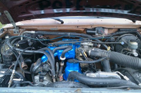 1987 Ford Bronco - The engine bay of a 1987 Ford Bronco, a prominent blue intake manifold and a SuperMotors watermark.
