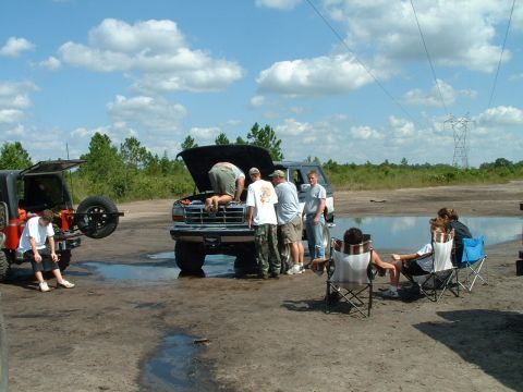 1995 Ford Bronco - Group works on a Ford Bronco's engine while others relax nearby in camping chairs.