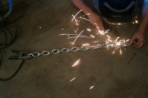 1987 Ford Bronco - A person is welding a heavy-duty metal chain, creating a shower of bright sparks.