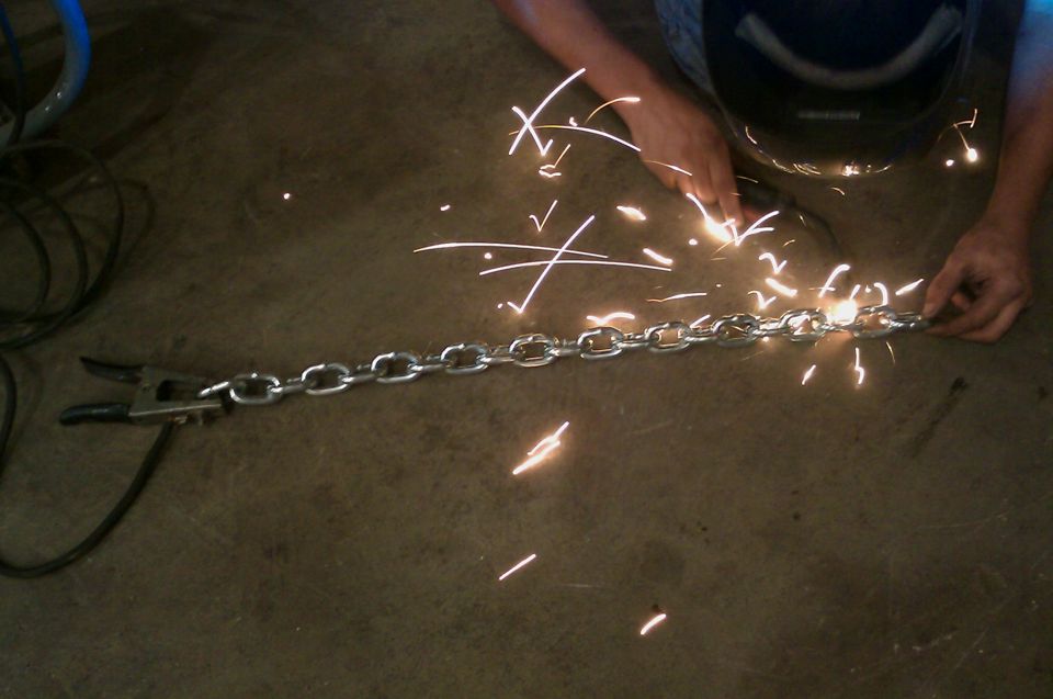 Person welding a metal chain on a concrete floor, sparks flying