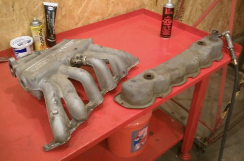 1987 Ford Bronco - Engine parts, an intake manifold and valve cover, sit on a red cart next to various automotive fluids.