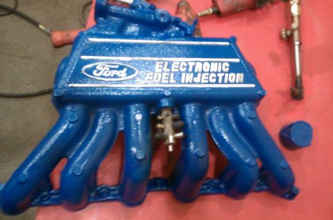 1987 Ford Bronco - A blue Ford Electronic Fuel Injection manifold is shown on a red surface, with tools in the background.