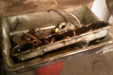 1987 Ford Bronco - A dirty oil pan and oil filter screen are shown in a metal tray, likely during an oil change or engine maintenance.
