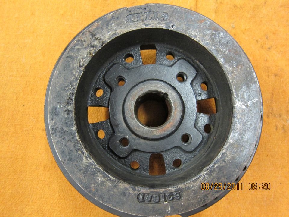 Metal automotive part with a central hub and bolt holes, showing rust and wear