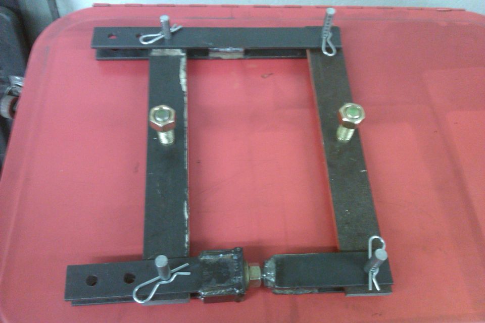 Black metal bracket with two bolts and two pins, resting on a red surface
