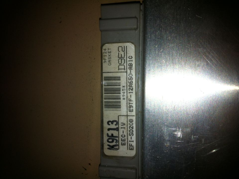 Gray engine control module with a white label showing part numbers and a barcode