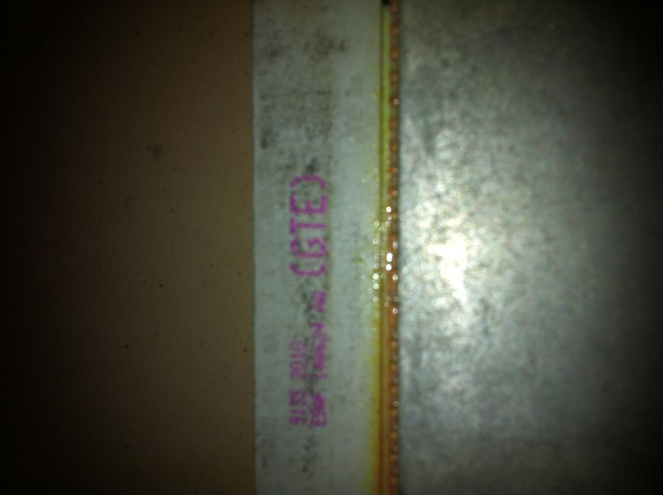 Close-up of a white trim piece with purple text that says "(GTE)" and some other faded markings