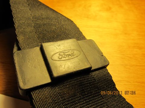 1969 Ford Mustang - A black seatbelt with a Ford emblem is shown against a wooden background.