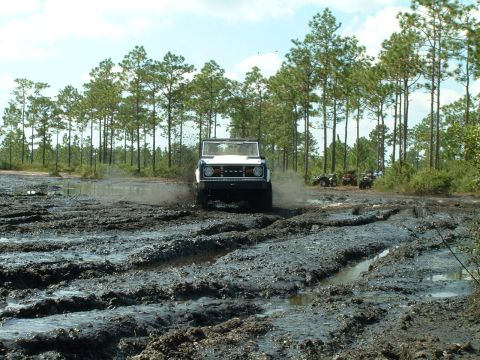 1995 Ford Bronco - SUV navigates a muddy track with ATVs visible in the background.