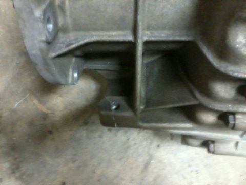 1985 Ford Bronco - A close-up view of a metal transmission housing, showing mounting points and bolts.