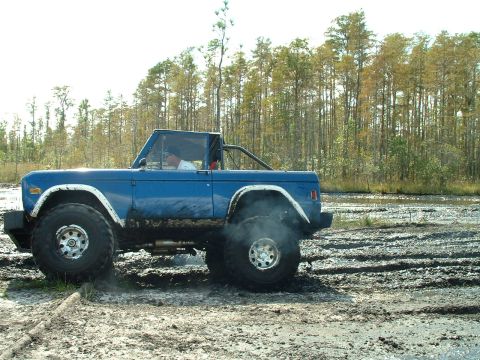 1995 Ford Bronco - Ford Bronco navigates a muddy terrain with trees in the background.