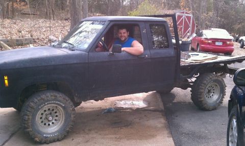 1988 Ford Ranger - A man sits in a black flatbed pickup truck, with a red car visible in the background.