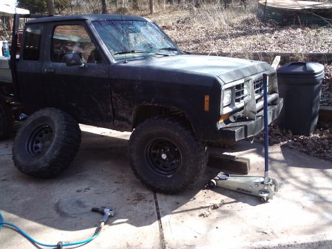 1988 Ford Ranger - A black pickup truck is shown with its front passenger side elevated by a hydraulic jack, suggesting maintenance or modification.