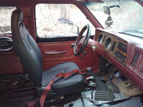 1988 Ford Ranger - The interior of an older model truck shows red door panels and a black bucket seat with a red seatbelt.
