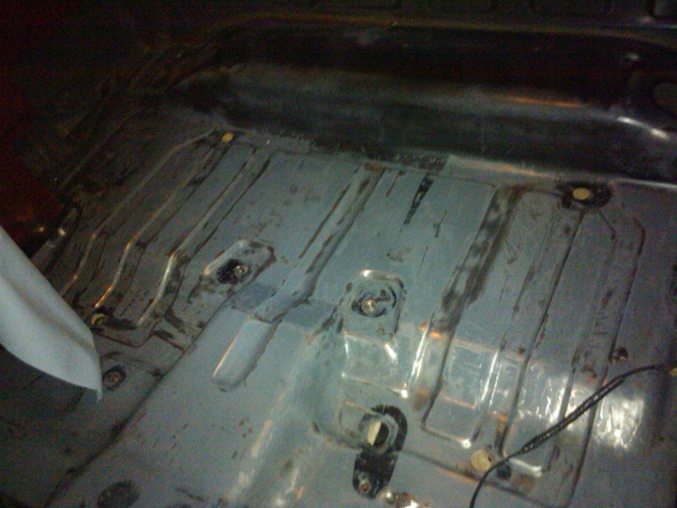 Interior floor of a vehicle, showing metal bracing and mounting points. A white object is on the left
