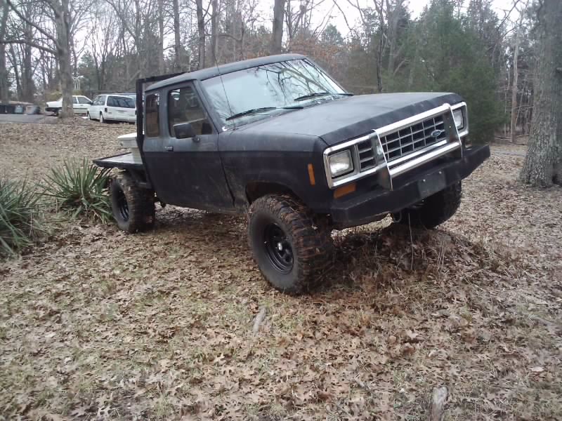 Black flatbed truck with off-road tires, angled on uneven terrain