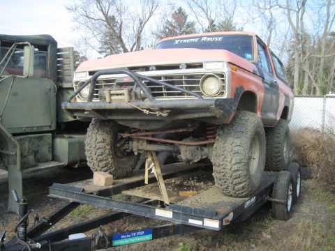 1978 Ford Bronco - This heavily modified SUV is loaded onto a trailer, parked next to a large military vehicle.