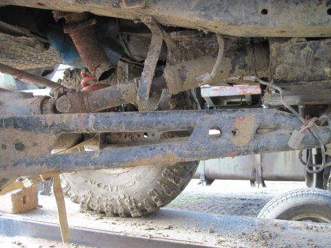 1978 Ford Bronco - The underside of a 4x4 vehicle shows its suspension, drive shaft, and a muddy tire.
