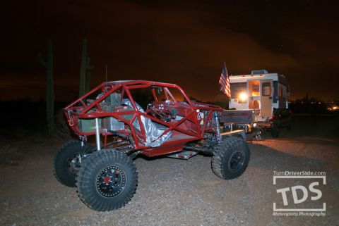 Suzuki Samurai - A custom-built red off-road buggy is parked next to a camper trailer under a dark sky.