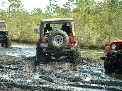 1995 Ford Bronco - Multiple Jeeps navigate a muddy trail, kicking up water and dirt.
