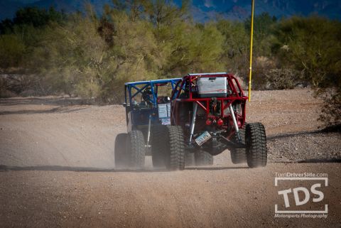 Suzuki Samurai - Two custom off-road buggies kick up dust as they drive along a dirt path in a desert landscape.