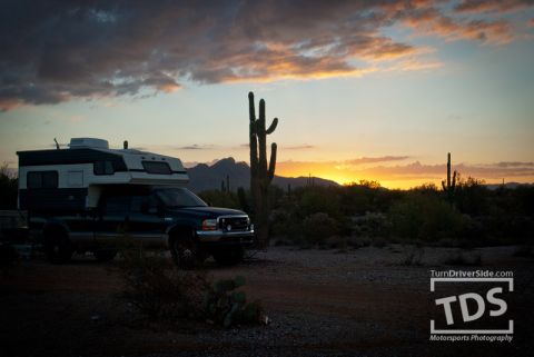 Suzuki Samurai - Pickup truck with camper shell parked in desert landscape at sunset with saguaro cacti.