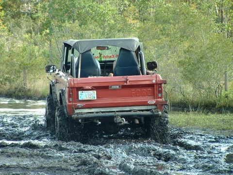 1995 Ford Bronco - This red Ford Bronco is navigating a muddy off-road course, kicking up mud as it goes.