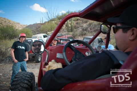 Suzuki Samurai - Driver and passenger in a red off-road buggy, with other vehicles visible in the desert landscape.