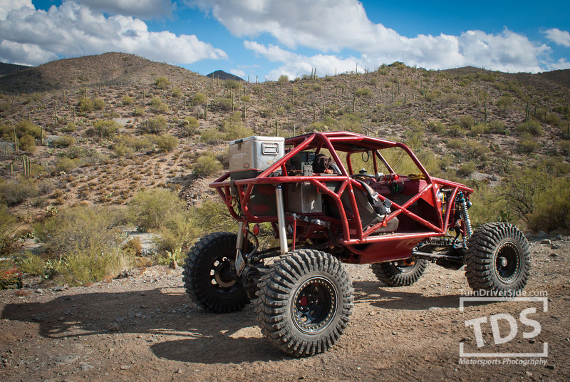 Red off-road buggy with a roll cage and large tires parked on a dirt road in a desert landscape