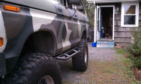 1979 Ford Bronco - Lifted 1978 Ford Bronco in camouflage paint sits beside a house with an open door.