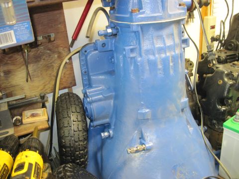 1978 Ford Bronco - A blue transmission part is visible alongside a spare tire and various tools, suggesting a workshop or repair setting.