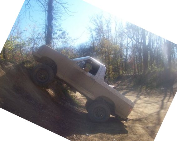 Pickup truck on a steep dirt incline, tires kicking up dirt. Looks like a mid-80s Ford Ranger