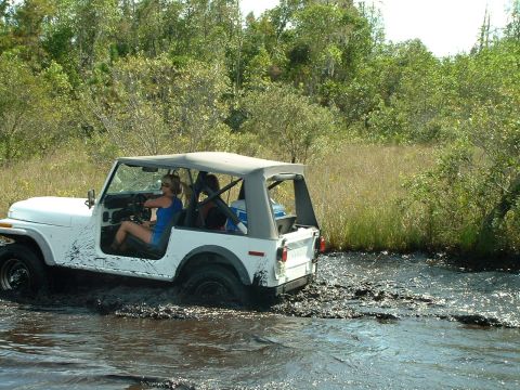 1995 Ford Bronco - A white Jeep Wrangler navigates through a muddy trail, with a woman at the wheel.