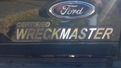 1993 Ford F-150 - Close-up of a Ford emblem and "Certified Wreckmaster" badge on the rear of a dark green truck.